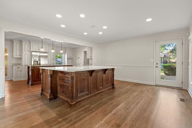 kitchen featuring crown molding, a sink, wood finished floors, stainless steel fridge, and a large island