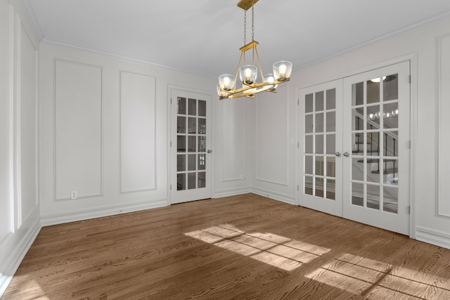 unfurnished dining area featuring french doors, an inviting chandelier, wood finished floors, a decorative wall, and ornamental molding