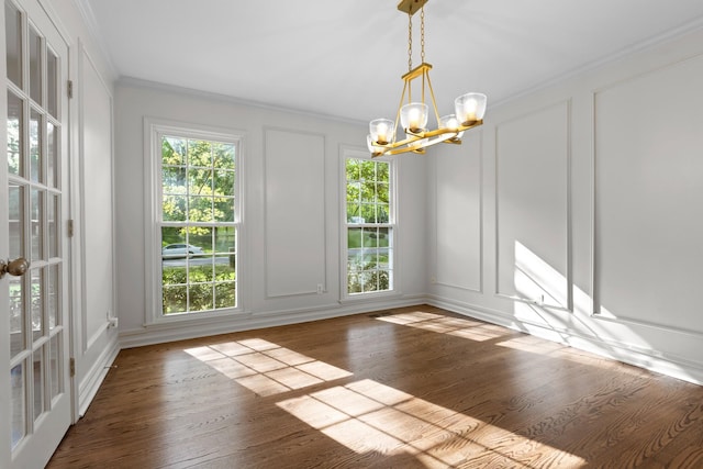 unfurnished dining area featuring a chandelier, wood finished floors, a decorative wall, and ornamental molding