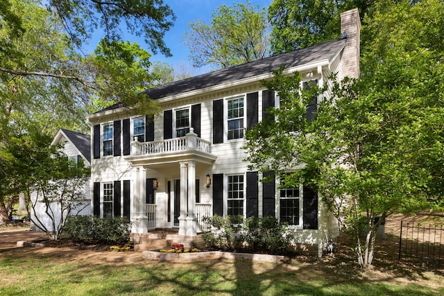 colonial-style house with a chimney, fence, and a front yard
