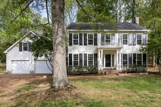 colonial house with a balcony, a chimney, driveway, an attached garage, and a front yard