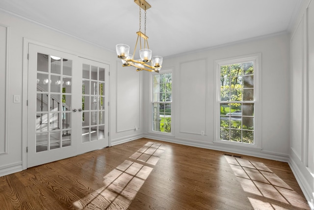 unfurnished dining area featuring wood finished floors, ornamental molding, and an inviting chandelier