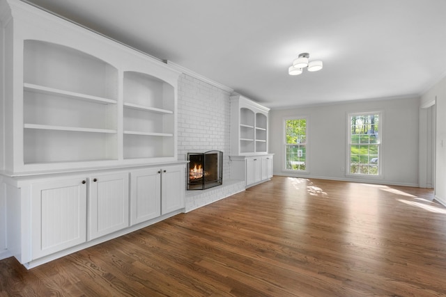 unfurnished living room featuring dark wood finished floors, a brick fireplace, built in shelves, and ornamental molding