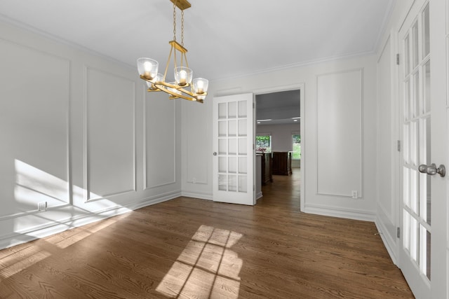unfurnished dining area with an inviting chandelier, ornamental molding, french doors, a decorative wall, and dark wood-style flooring