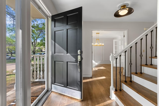 foyer with stairway, an inviting chandelier, and wood finished floors