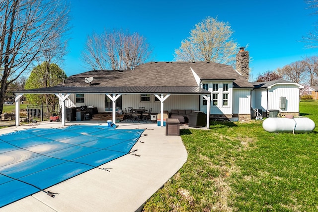 rear view of property with an outdoor hangout area, a patio, a chimney, a covered pool, and a yard