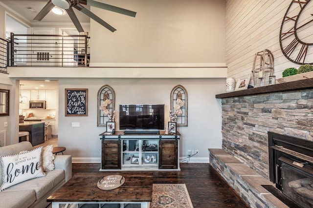 living area featuring hardwood / wood-style flooring, ornamental molding, ceiling fan, a stone fireplace, and a high ceiling