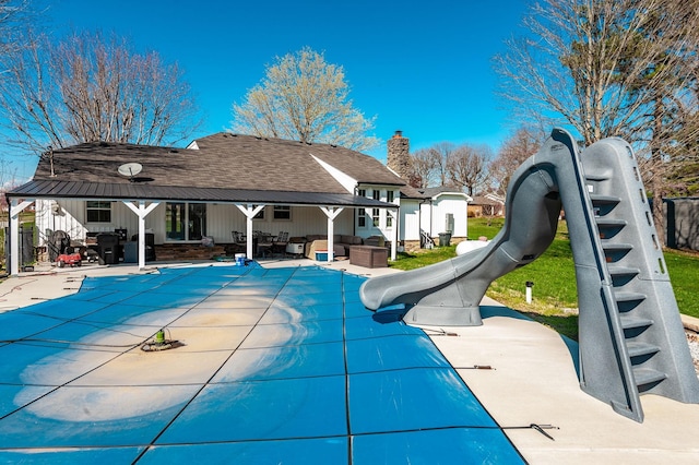 view of pool featuring a patio, an outdoor hangout area, a water slide, a covered pool, and fence