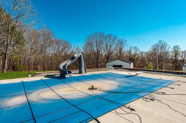 view of swimming pool featuring a patio area, a water slide, a covered pool, an outbuilding, and a diving board