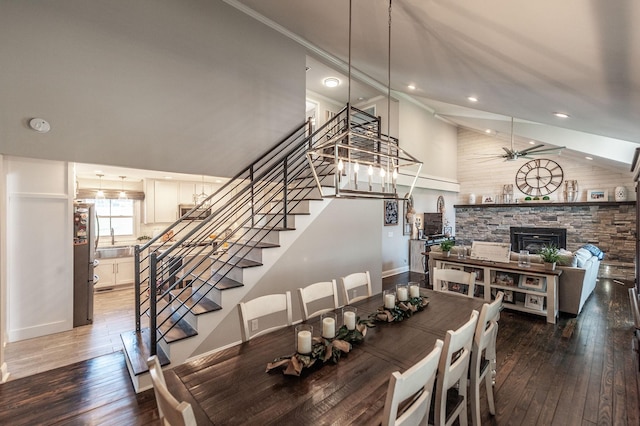 dining room with stairs, a stone fireplace, high vaulted ceiling, and hardwood / wood-style flooring