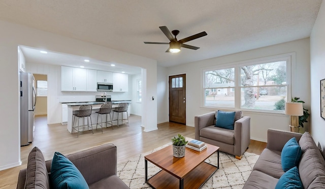 living room with baseboards, light wood-type flooring, and a ceiling fan
