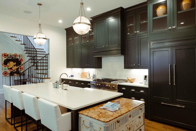 kitchen with light countertops, wood finished floors, high end stainless steel range oven, an island with sink, and hanging light fixtures