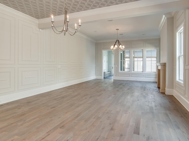 interior space with an inviting chandelier, a decorative wall, crown molding, and light wood finished floors