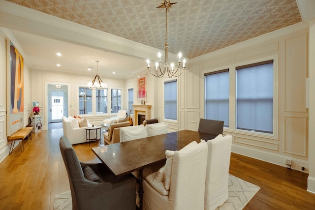 dining room featuring an inviting chandelier, a decorative wall, ornamental molding, and light wood-type flooring