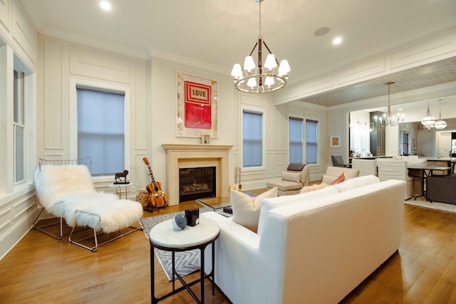 living area featuring a glass covered fireplace, wood finished floors, a decorative wall, and an inviting chandelier