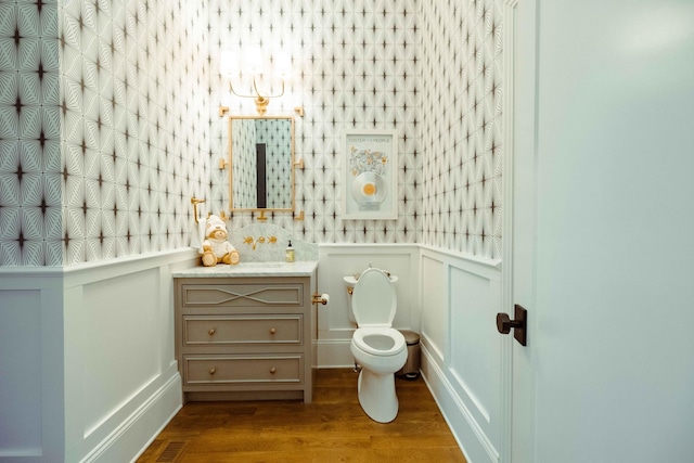 half bath with a decorative wall, visible vents, toilet, wood finished floors, and vanity