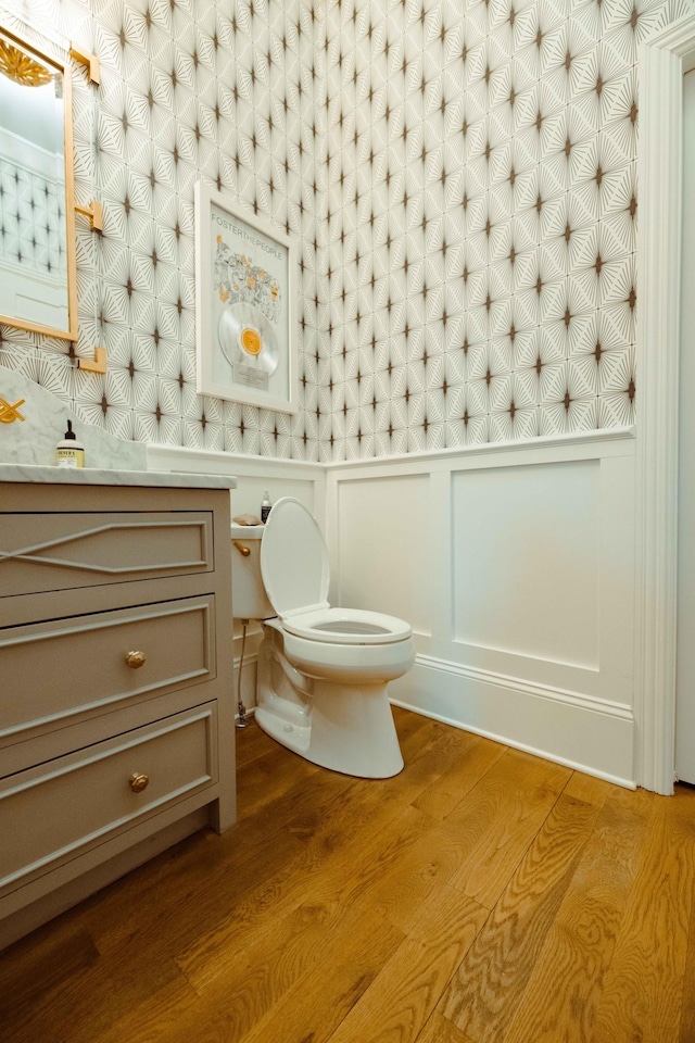 bathroom with a decorative wall, toilet, vanity, and wood finished floors