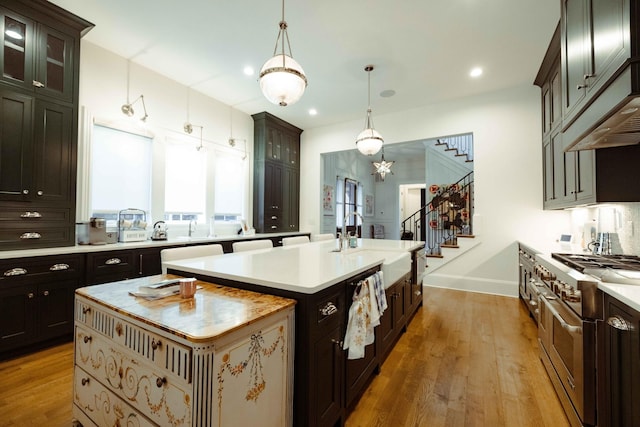 kitchen with light countertops, a kitchen island with sink, high end stainless steel range, and light wood finished floors