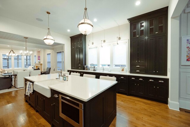 kitchen with light countertops, a sink, a healthy amount of sunlight, light wood-type flooring, and a notable chandelier