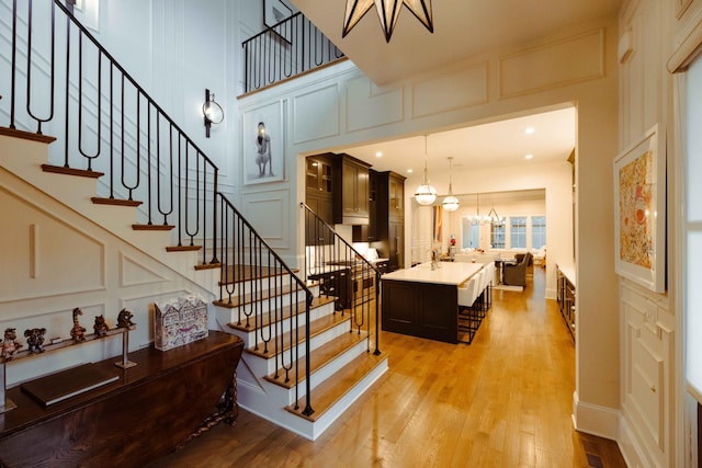 staircase featuring a high ceiling, a decorative wall, a notable chandelier, and wood finished floors
