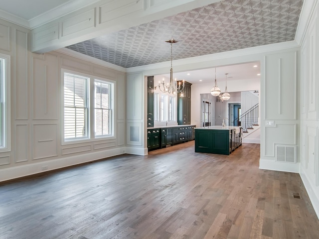 kitchen with light countertops, a decorative wall, visible vents, ornamental molding, and an inviting chandelier