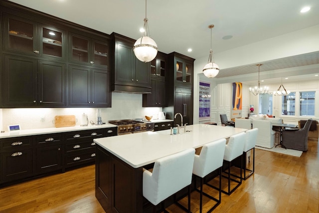 kitchen with light countertops, a breakfast bar area, an inviting chandelier, high end stainless steel range, and light wood finished floors