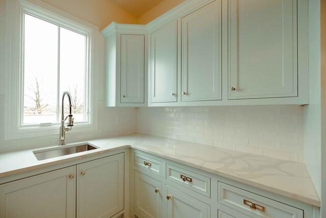 kitchen featuring backsplash, a sink, white cabinetry, and light stone counters