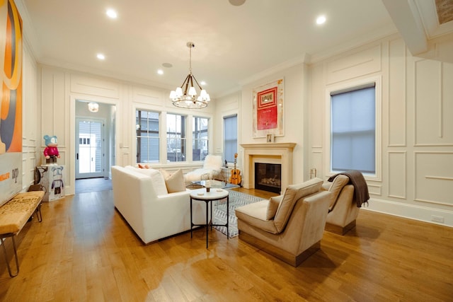 living area with a notable chandelier, light wood-style floors, ornamental molding, and a decorative wall