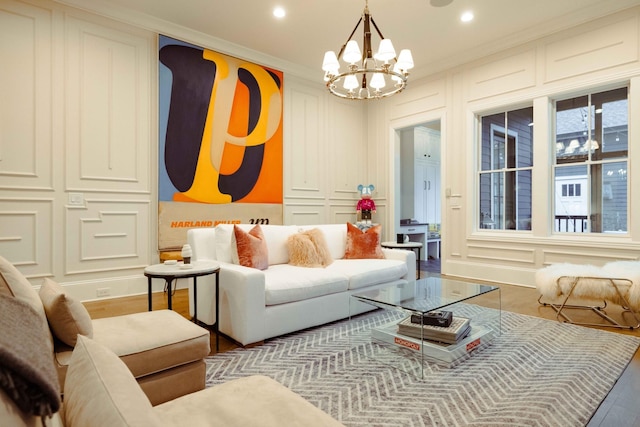 living room featuring wood finished floors, a decorative wall, ornamental molding, recessed lighting, and an inviting chandelier