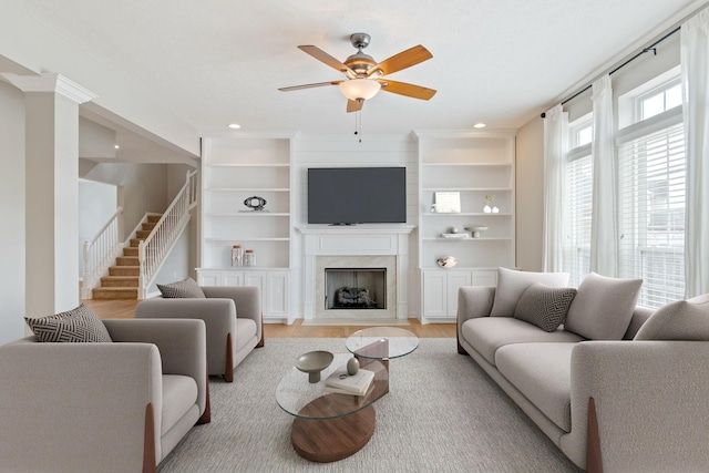 living room featuring ceiling fan, a fireplace, stairway, recessed lighting, and light wood-style flooring