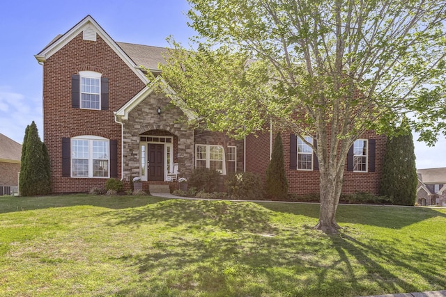 traditional home featuring brick siding, stone siding, and a front lawn