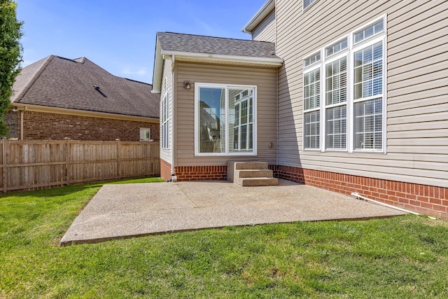entrance to property featuring a yard, a patio area, a shingled roof, and fence