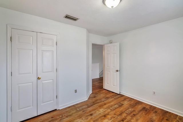 unfurnished bedroom featuring wood finished floors, a closet, baseboards, and visible vents
