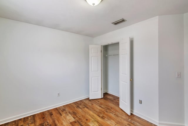 unfurnished bedroom featuring baseboards, visible vents, a closet, and wood finished floors