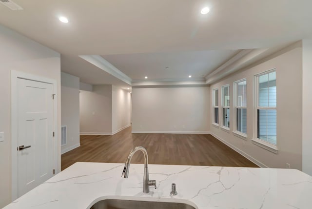 kitchen with a sink, wood finished floors, a raised ceiling, baseboards, and recessed lighting