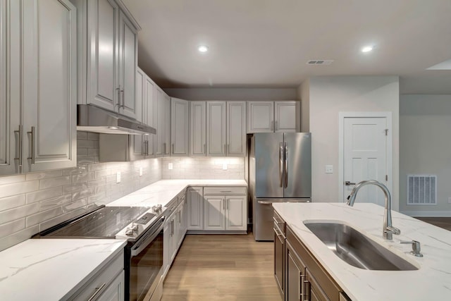 kitchen featuring appliances with stainless steel finishes, a sink, under cabinet range hood, light wood finished floors, and recessed lighting