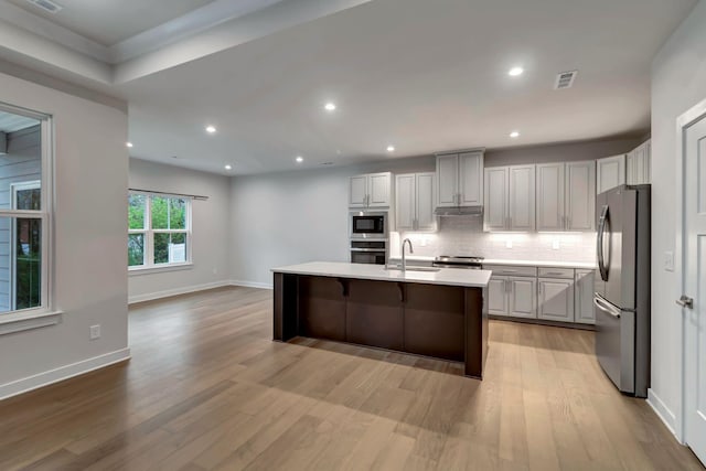 kitchen featuring stainless steel appliances, a sink, light wood finished floors, decorative backsplash, and light countertops