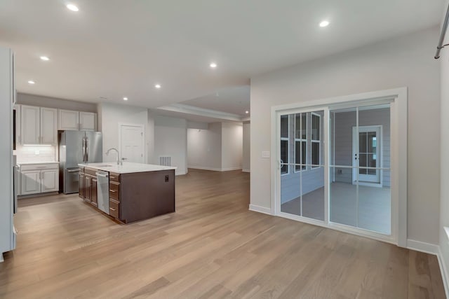 kitchen with stainless steel appliances, open floor plan, light countertops, light wood-style floors, and baseboards