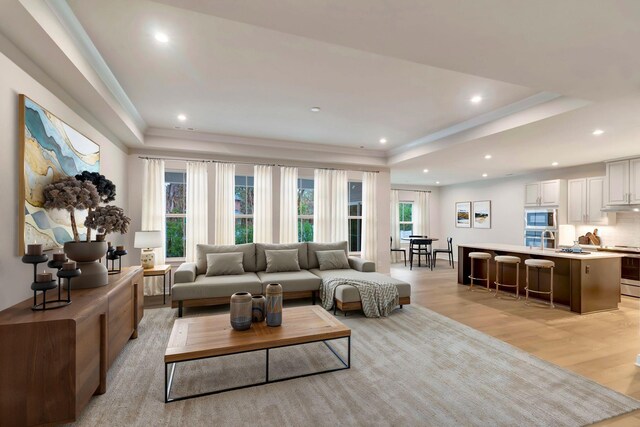 living room with a raised ceiling, light wood finished floors, ornamental molding, and recessed lighting