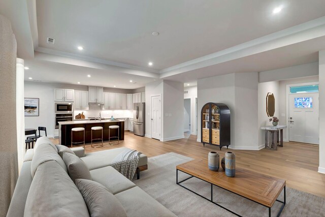 living room with a raised ceiling, light wood-style floors, recessed lighting, and baseboards