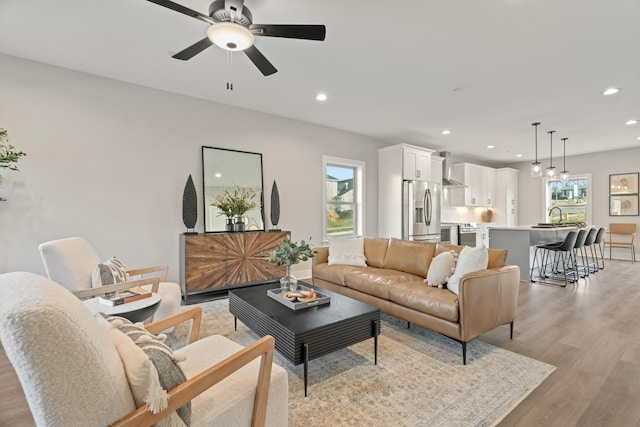 living area featuring baseboards, light wood-type flooring, ceiling fan, and recessed lighting
