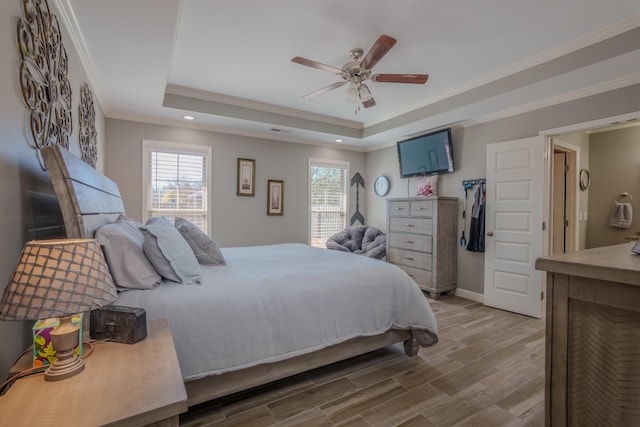 bedroom with ornamental molding, wood finished floors, multiple windows, and a raised ceiling