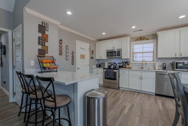 kitchen with a kitchen breakfast bar, light wood-style flooring, white cabinetry, and appliances with stainless steel finishes