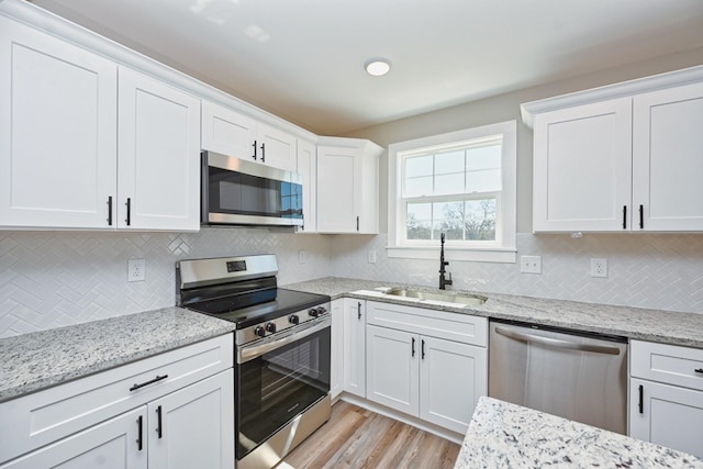 kitchen featuring stainless steel appliances, a sink, light wood finished floors, white cabinets, and light stone countertops