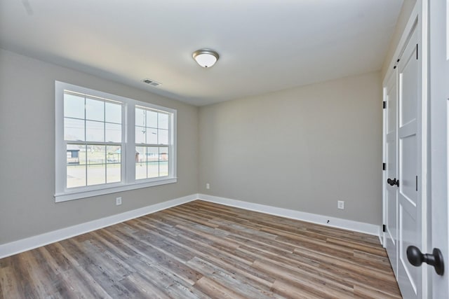 spare room with baseboards, visible vents, and wood finished floors