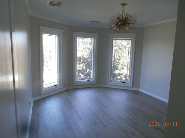unfurnished room with visible vents, baseboards, ornamental molding, wood finished floors, and an inviting chandelier