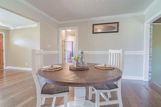 dining room with baseboards, a textured ceiling, crown molding, and wood finished floors