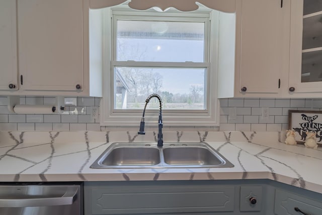 kitchen with glass insert cabinets, tasteful backsplash, a sink, and dishwasher