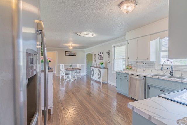 kitchen with a sink, crown molding, wood finished floors, and appliances with stainless steel finishes