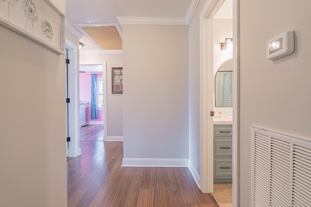 corridor featuring visible vents, ornamental molding, baseboards, and wood finished floors